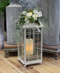 a white candle in a metal cage with flowers and greenery