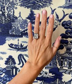 a woman's hand with a diamond ring on top of her left hand, against a blue and white background