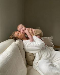 a woman laying on top of a bed holding a baby in her arms and kissing her cheek