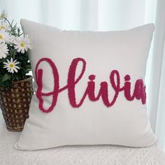 a white pillow with the word flavia on it next to a potted plant