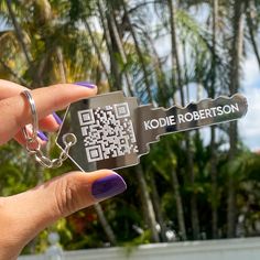 a hand holding a qr code keychain in front of some palm trees