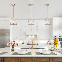 a large kitchen with white cabinets and stainless steel appliances, along with flowers in vases on the island