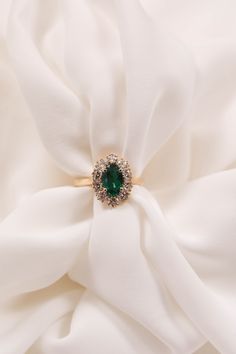 a close up view of a ring with a green stone surrounded by white satin fabric