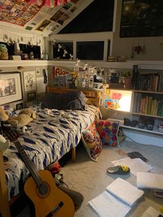 a bed room with a guitar on the floor next to a book shelf and books