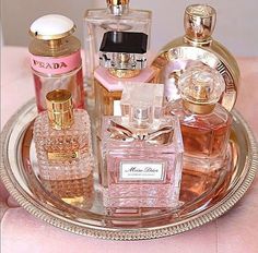 an assortment of perfume bottles sitting on a silver platter with pink velvet material and gold trim