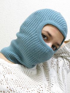 a woman wearing a blue knitted ski mask covering her face with a white sweater