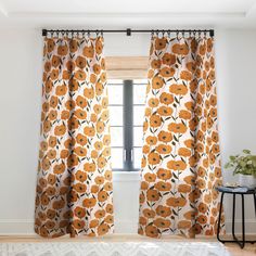 an orange flowered curtain hangs in front of a window with white walls and wooden floors