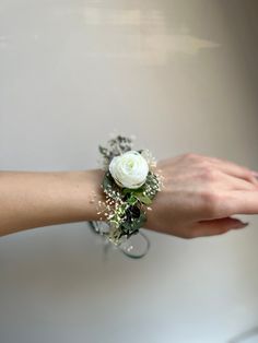 a woman's hand holding a white rose and baby's breath bracelet