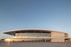 an empty parking lot in front of a large building with a curved roof and glass windows