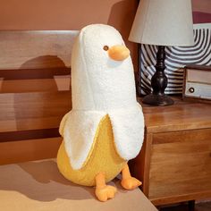 a stuffed penguin sitting on top of a wooden chair next to a lamp and table