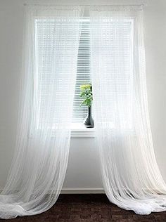 a vase with a flower in it sitting on a window sill next to a curtain