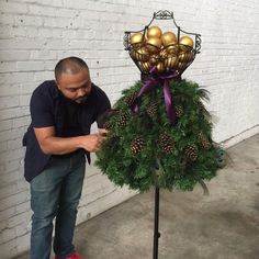 a man decorating a christmas tree with gold balls and pineconis on it