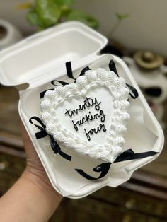 a heart shaped cake in a white box with black ribbon around the edges and writing on it