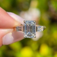 a woman's hand holding an engagement ring with three baguettes on it