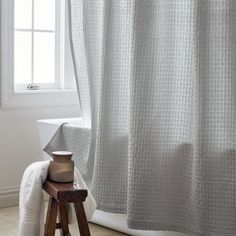 a white shower curtain sitting next to a wooden stool in front of a bathroom window