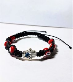 Carefully hand braided bracelet with charms that work as negativity shields. It is made with strong Black nylon thread and vibrant red evil eye beads ( represent courage and protection). The Hamsa hand is also a charm of protection and fortune caller as you can see it comes with a 2 mm evil eye in the middle (color blue, is the traditional color for good karma, positive energies, and protection against the evil eye.) When is finally made, the bracelet is then aligned with the wearer's name, an a Handmade Red Symbolic Beaded Bracelets, Adjustable Symbolic Bracelets For Festivals, Adjustable Symbolic Bracelets For Festival, Symbolic Adjustable Bracelets For Festivals, Symbolic Adjustable Friendship Bracelets, Adjustable Red Hand Wrapped Friendship Bracelets, Red Symbolic Handmade Bracelets, Handmade Red Braided Bracelets For Festival, Adjustable Hand Wrapped Evil Eye Bracelet