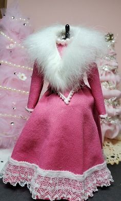 a pink dress with white fur collar and lace trims on the skirt is next to a pink christmas tree