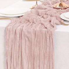 the table is set with white plates and pink linens on it, along with gold chargers