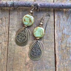 Boho brass and earthy green Czech glass dangle earrings.Small and lightweight, these brass earrings feature a small, swirled, earthy green and brown Czech glass bead and various shapes of brass dangles. The warm, light and neutral colors of these earrings make them a perfect everyday pair.Product overview:- Made with small Czech glass beads with various shapes of antiqued brass- Total hanging length of 2", the glass beads are approximately 0.5" in diameter- Very light weight and versatile- Hypoa Artisan Green Brass Earrings, Earthy Metal Dangle Earrings, Earthy Brass Dangle Earrings, Green Brass Earrings Nature-inspired, Rustic Brass Drop Earrings, Nickel-free Brass Earthy Earrings, Rustic Brass Dangle Earrings, Earthy Nickel-free Brass Earrings, Earthy Bronze Earrings With Ear Wire