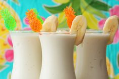 three glasses filled with milk and banana slices on top of each other, sitting in front of a colorful background