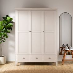 a white armoire next to a mirror and potted plant in a room with hardwood floors