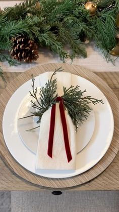 the table is set for christmas dinner with pine cones and greenery on it, along with napkins