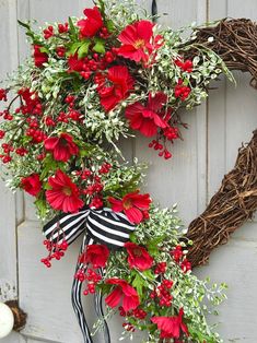 a wreath with red flowers and greenery hanging on a door