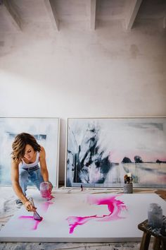 a woman is painting on the floor in front of two paintings with pink spray paint