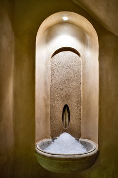 an indoor fountain with water running from it's sides into the ground, in front of a round window