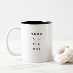 two donuts sitting next to each other on a white table with the words shuh duh fuh cup