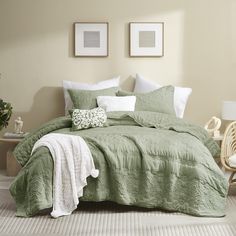 a bed with green comforter and pillows in a room next to two pictures on the wall