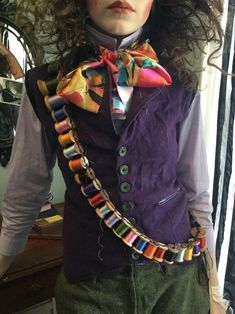 a young boy wearing a purple vest and tie with colorful buttons on the front, while standing next to a mirror