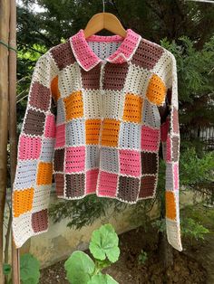 a crocheted jacket hanging on a clothes line in front of some trees and bushes