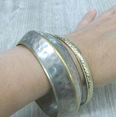 "A pair of matching Vintage brass bracelets in boho style, can be worn as a set or each one separately. These bracelets were a travel souvenir from India, made in the 1980s. Wide bracelet: silver plated brass, 14 mm wide and 6-7 mm thick with textured hammered surface and a rib around the middle. The silver plate is a bit worn off, the edges and the rib looks gold color. Narrow bracelet: 6 mm wide, gold plated brass with textured surface, the pattern looks like flowers and leaves. Length: 8 inch Brass Bangle, Wide Bracelet, Brass Bracelet, Travel Souvenirs, Gold Plated Bracelets, Boho Bracelets, Silver Bracelets, Vintage Brass, Gold Color