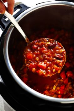 a ladle full of chili and beans is being stirred with a wooden spoon in the slow cooker