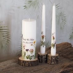 three white candles sitting on top of wooden logs next to each other with flowers painted on them