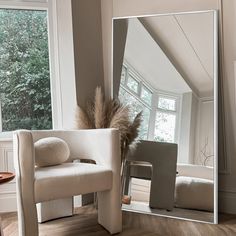 a large mirror sitting on top of a wooden floor next to a chair and window