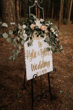 a wedding sign with flowers and greenery is displayed on a stand in the woods