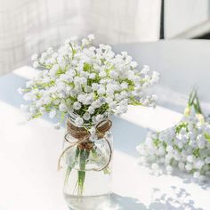 a glass vase filled with white flowers sitting on top of a table next to another vase