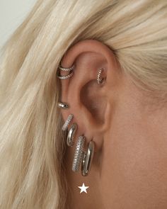 a woman with blonde hair wearing three silver rings and two star ear cuff earrings on her left ear