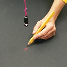 a person holding a pencil and writing on a black surface with a pink string attached to it