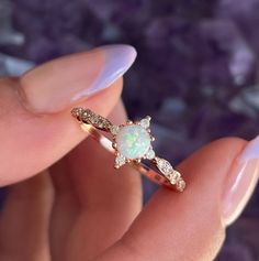 a woman's hand holding an opal and diamond ring