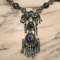 "A fun, elaborate, long, \"statement piece\" necklace. The bottom pendant has a blue glass eye or \"evil eye\" motif and measures with metal setting 1 1/8\" in diameter. Pendant length is a good 2 1/4\" with fringe. The style looks Indian (from India), complete with beaded fringe and intricate chain work. The chain is enhanced with several 5/8\" diameter disks embedded with blue and green glass rhinestones in various patterns. The bottom three disks also have beaded fringe. The metal work is sil Eye Motif, Enamel Locket, Rhinestone Jewelry Set, Glass Bracelet, Hanging Earrings, Necklace Boho, Beaded Fringe, Metal Work, Green Necklace