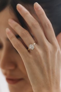 a woman holding her hand up to her face with a diamond ring on it's finger