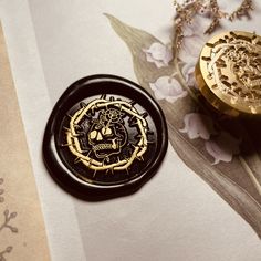 two gold and black buttons sitting on top of a piece of paper next to flowers