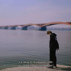 a woman standing on the edge of a cliff next to water with a bridge in the background