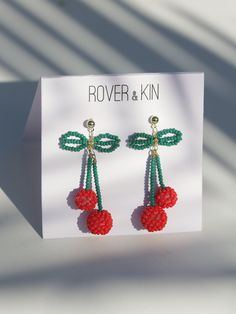 a pair of red and green beaded cherries hanging from earrings on a card