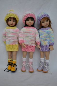 three dolls standing next to each other wearing knitted clothes and hats, all in different colors