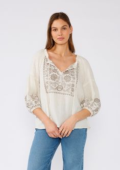 [Color: Natural/Taupe] A front facing image of a brunette model wearing an ivory flowy bohemian peasant top with embroidered detail and tassel ties. Bohemian V-neck Blouse With Embroidered Hem, Beige Linen Tops With Floral Embroidery, Bohemian V-neck Embroidered Top, Fall Linen Tops With Floral Embroidery, Traditional Embroidered V-neck Peasant Top, Folk Style V-neck Blouse With Embroidered Neckline, Floral Embroidered Linen Tops For Fall, Linen Tops With Floral Embroidery For Fall, Summer Embroidered V-neck Peasant Top