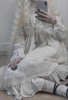 a woman with long white hair sitting on the floor while holding a cell phone in her hand